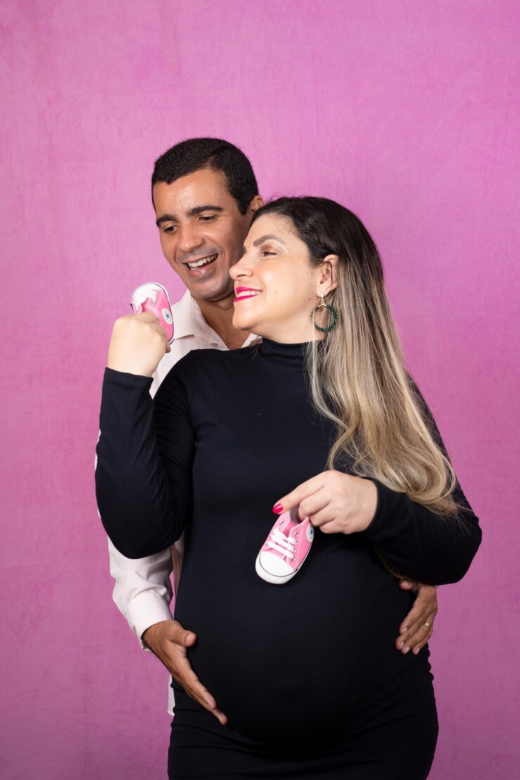 Foto casal romântico de marido bonito e linda esposa grávida posando no estúdio ela segura chinelos de bebê