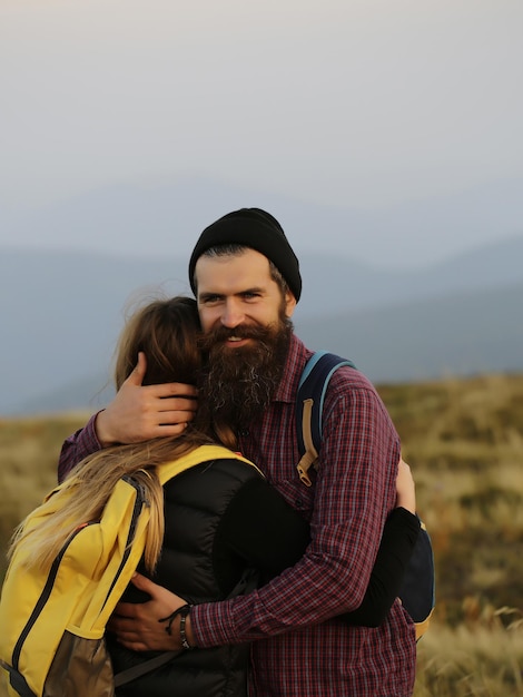 Casal romântico de mulher ou menina e homem barbudo bonito abraçam-se no penhasco sobre os topos das montanhas ao ar livre com mochila amarela