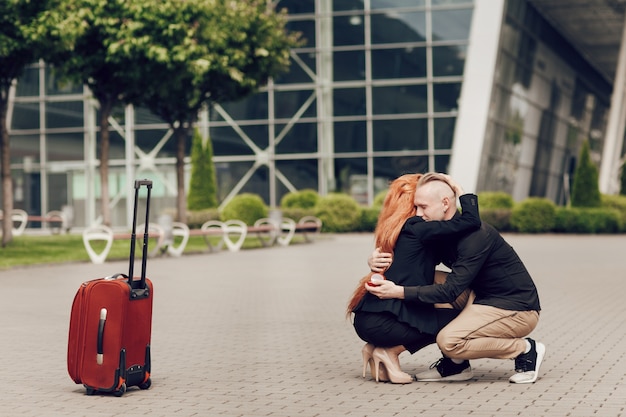 Casal romântico em pé perto do aeroporto com uma mala