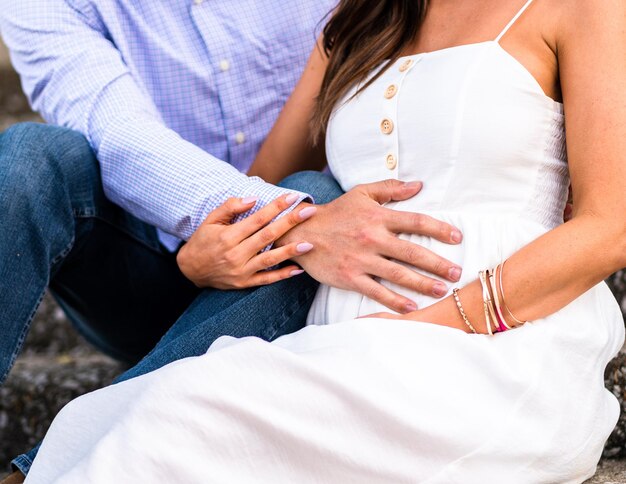 Foto casal romântico grávido relaxando ao ar livre; uma mão de homem tocando a barriga da mulher