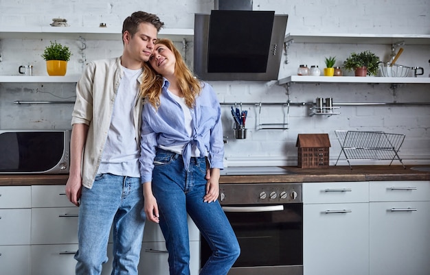 Casal romântico na cozinha de casa. uma mulher bonita e um homem atraente se divertem em pé na cozinha e se abraçando