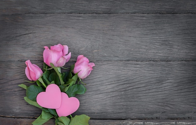 Casal rosa de corações e rosas cor de rosa em fundo de madeira