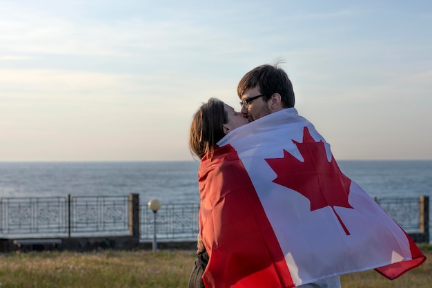 Casal se beijando escondido atrás da bandeira da paixão do Canadá