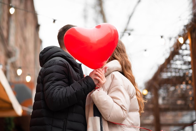 Casal segurando um balão em forma de coração e beijando na rua. Conceito de dia dos namorados, presentes, amor