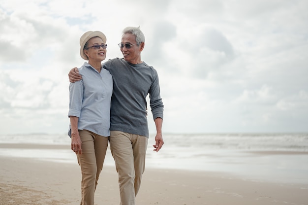 Casal sênior abraça caminhar na praia, plano de seguro de vida com o conceito de feliz aposentadoria.