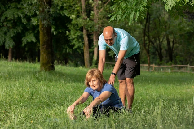 Casal sênior ajudando a mulher a ganhar flexibilidade enquanto relaxa na grama no ambiente natural