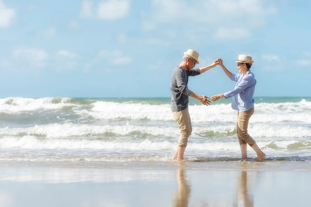 Casal sênior asiático dançando na praia. lua de mel idosa juntos muito felicidade após a aposentadoria. plano de seguro de vida. atividade após a aposentadoria no verão