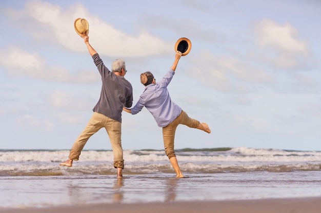 Foto casal sênior asiático pulando na praia. lua de mel idosa juntos muito felicidade após a aposentadoria. plano de seguro de vida. atividade após a aposentadoria no verão