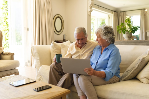 Foto casal sênior caucasiano sentado no sofá usando laptop. retiro, aposentadoria e conceito de estilo de vida sênior feliz.