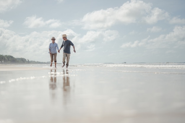 Casal sênior correndo na praia em dia ensolarado. planeje o seguro de vida com o conceito de uma aposentadoria feliz.