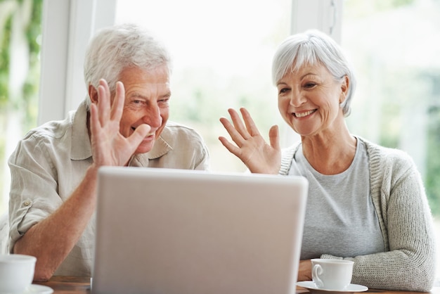 Casal sênior laptop e acenando na videochamada comunicação digital e conexão voip em casa Feliz velho idoso e acenar olá no computador para contato virtual rede online e bate-papo