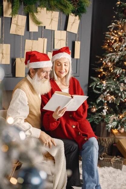 Casal sênior lendo um livro juntos, sentado perto da árvore de natal