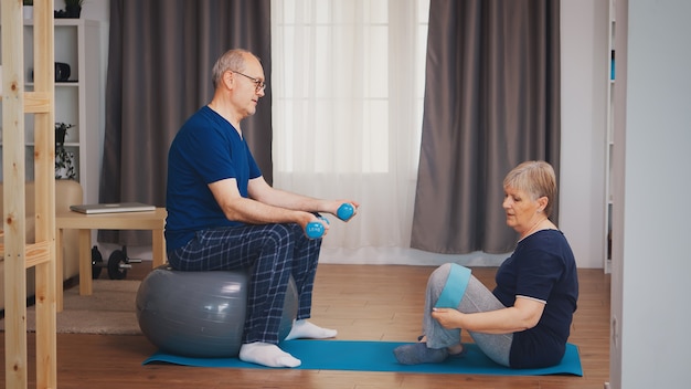 Casal sênior na sala de estar fazendo treinamento físico no tapete de ioga e bola de estabilidade. Idoso estilo de vida saudável, exercícios em casa, exercícios e treinamento, atividades esportivas em casa