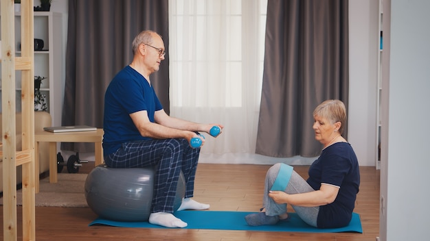 Casal sênior na sala de estar fazendo treinamento físico no tapete de ioga e bola de estabilidade. idoso estilo de vida saudável, exercícios em casa, exercícios e treinamento, atividades esportivas em casa