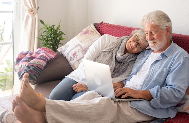 Casal sênior relaxado em casa usando o laptop. Dois idosos aposentados aproveitando seu tempo livre e aparelhos tecnológicos