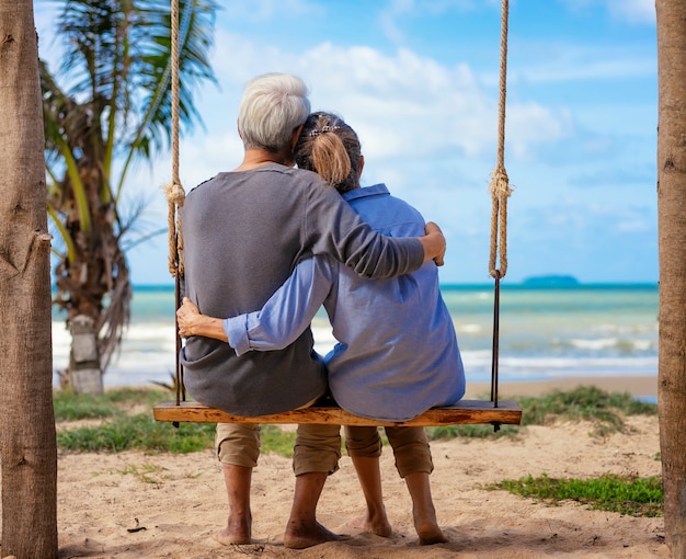 Foto casal senior sentado em um balanço na praia