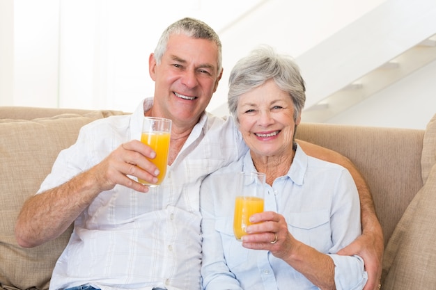 Casal sênior sentado no sofá bebendo suco de laranja