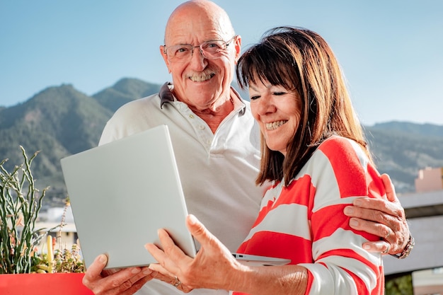 Casal sênior sorridente ao ar livre usando computador portátil juntos desfrutando de férias e viagens