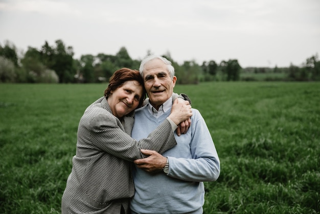 Casal sênior sorridente feliz apaixonado pela natureza, se divertindo. Casal de idosos no campo verde. Casal sênior fofo caminhando e se abraçando na floresta de primavera