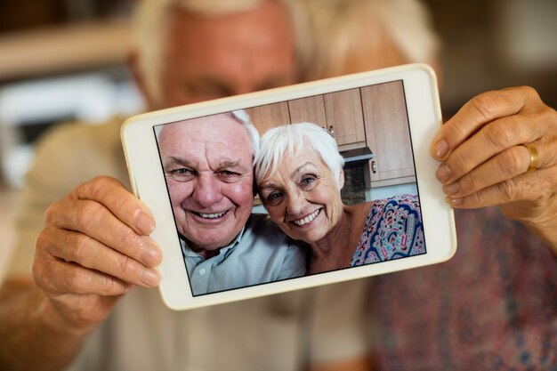 Casal sênior tirando selfie com tablet digital na cozinha de casa