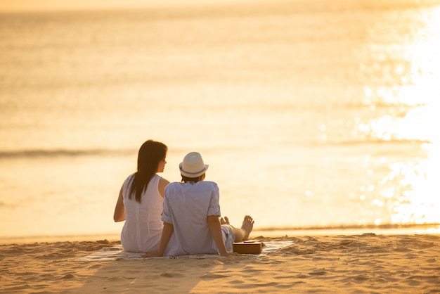 Casal senta-se na areia, olhando para o mar juntos.