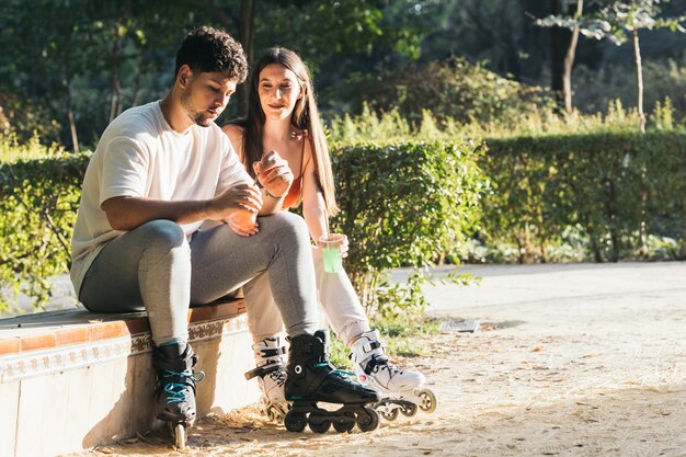 Casal sentado em um parque bebendo refrigerante usando patins