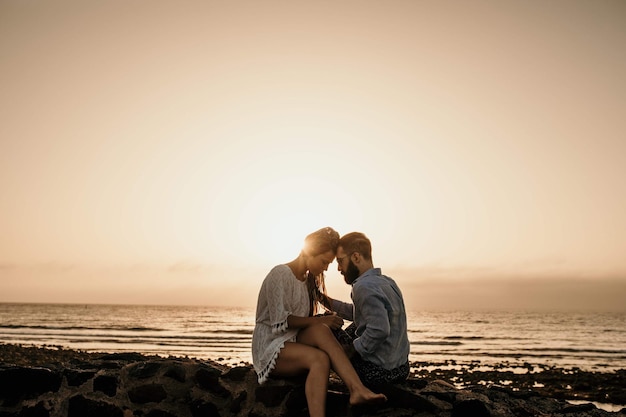 Casal sentado em uma rocha na praia durante o pôr do sol