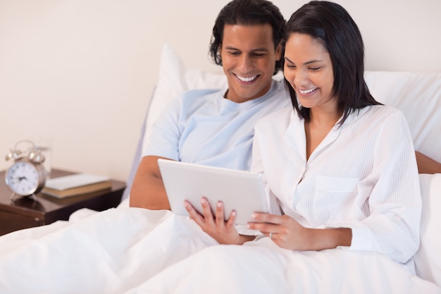 Casal sentado na cama usando tablet pc