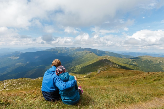 Casal sentado na colina da montanha, abraçando-se e olhando para a paisagem, homem e mulher romântico