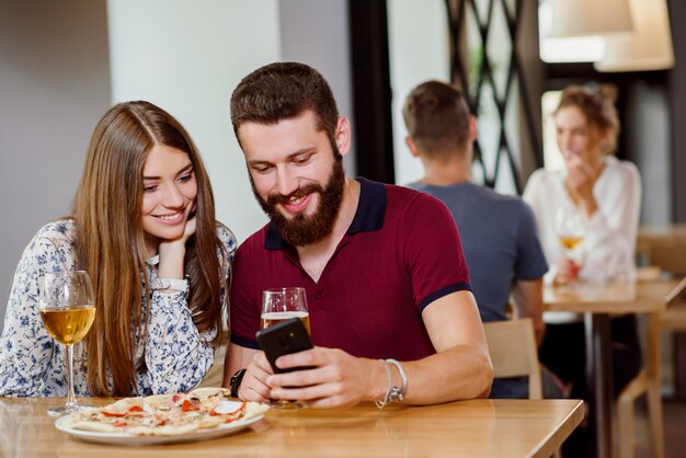 Casal sentado na pizzaria com pizza, vinho e cerveja.