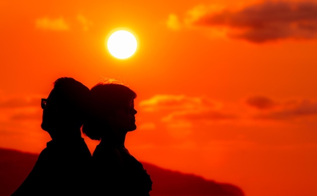 Foto casal sentado na praia silhueta no pôr do sol amor e amizade de costas para trás