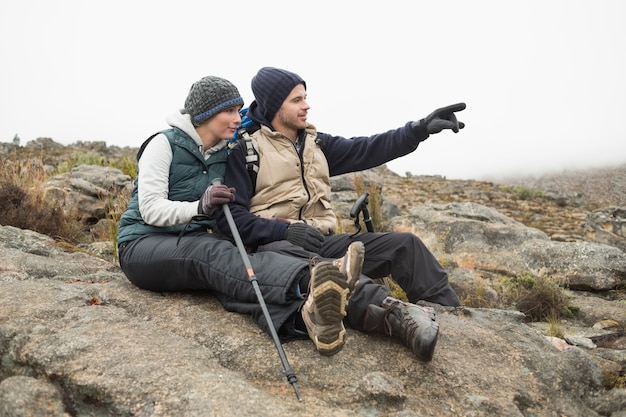 Casal sentado na rocha com bastões trekking enquanto faz uma caminhada