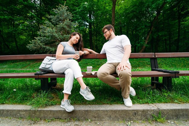 Casal sentado no banco conversando e tomando café no parque