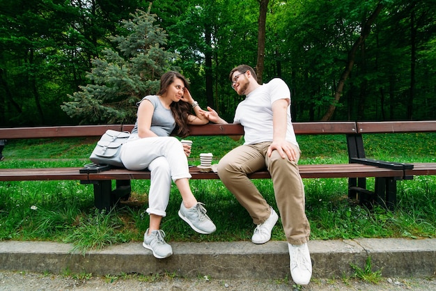 Casal sentado no banco conversando e tomando café no parque