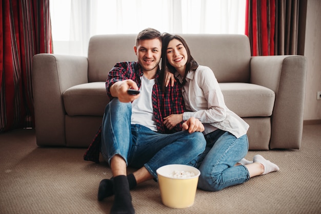 Foto casal sentado no chão assistindo tv com pipoca
