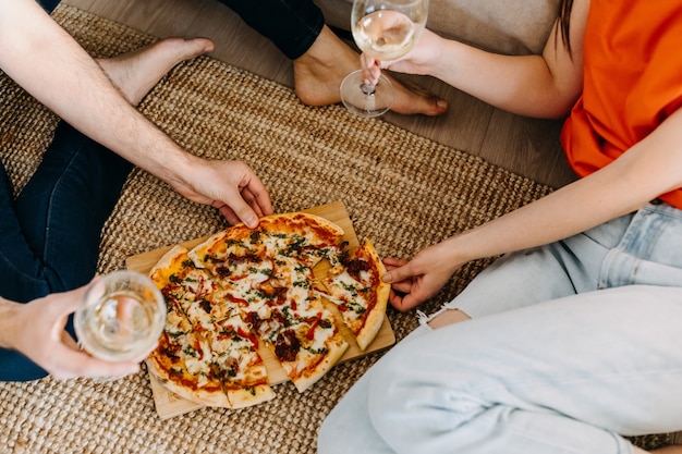 Casal sentado no chão, comendo pizza e bebendo vinho