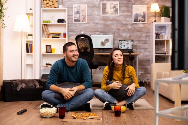 Casal sentado no chão e assistindo tv na sala de estar.