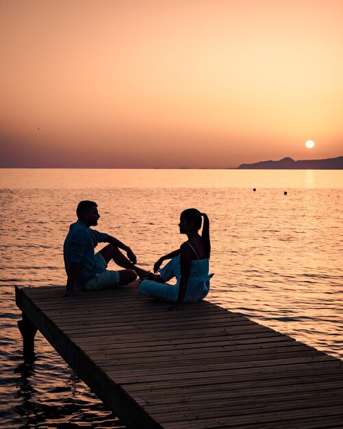 Foto casal sentado no mar contra o céu durante o pôr-do-sol