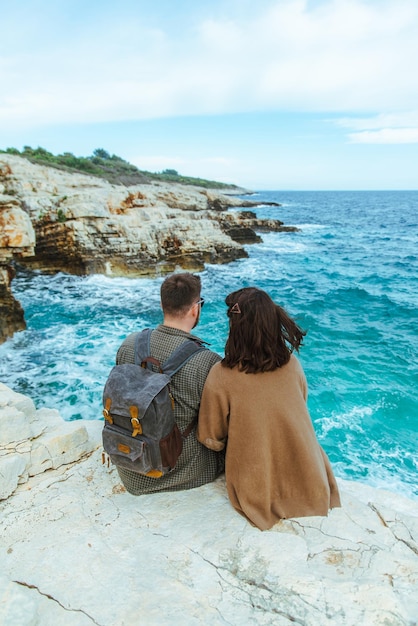 Casal sentado no penhasco olhando as ondas grandes do mar