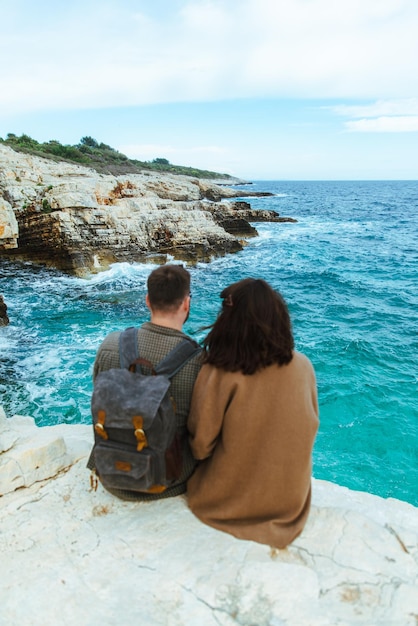 Casal sentado no penhasco olhando para o mar