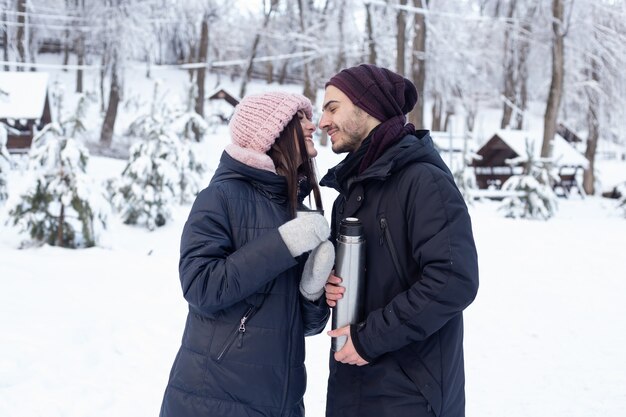 Casal servindo chá de uma garrafa térmica no parque de inverno