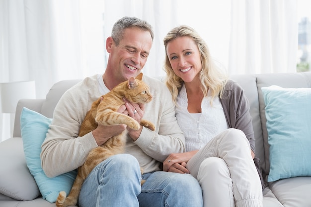 Casal sorridente acariciando seu gato gringer no sofá