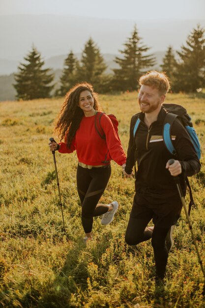 Casal sorridente andando com mochilas sobre colinas verdes