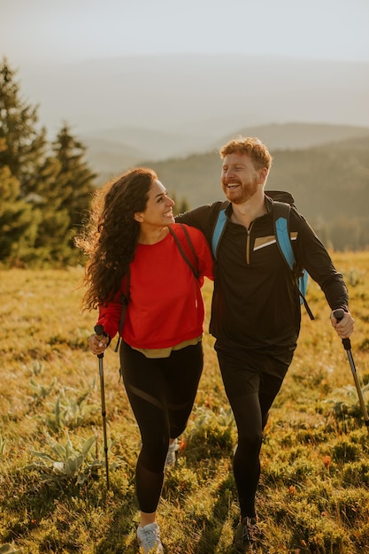 Casal sorridente andando com mochilas sobre colinas verdes