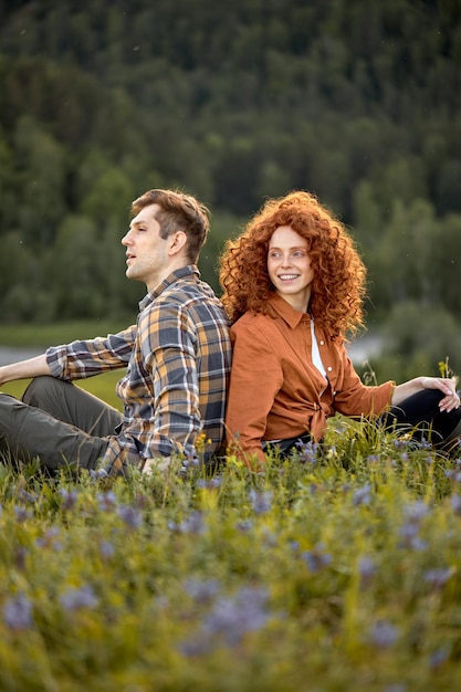 Casal sorridente, caminhadas nas montanhas de verão na zona rural. Homem e mulher felizes sentam-se na grama. Turistas femininos e masculinos em trajes casuais, explorando a natureza. Retrato da vista lateral. Natureza, conceito de pessoas