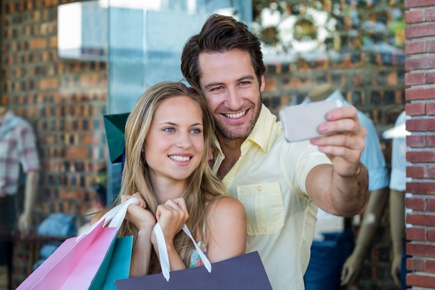 Foto casal sorridente com sacolas de compras tendo selfies