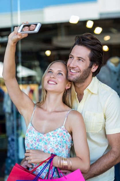 Casal sorridente com sacolas de compras tendo selfies