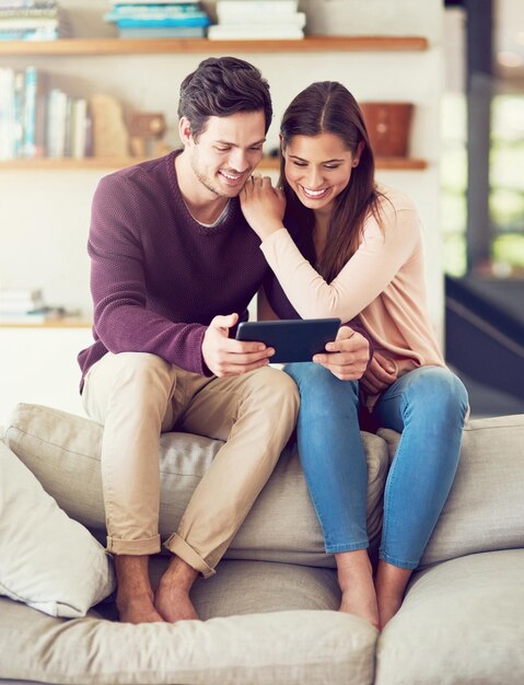 Casal sorridente e relaxante no sofá com tablet para notícias de mídia social ou streaming de vídeo juntos Tecnologia digital homem e mulher na sala de estar para compras on-line ou ler blog em aplicativo em casa