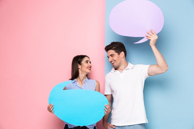 Foto casal sorridente segurando bolhas de copyspace para anúncio, isolado sobre uma parede colorida