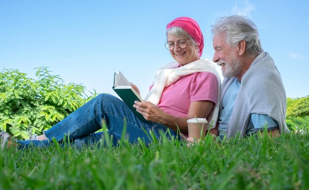 Casal sorridente sênior sentado na grama no parque público tendo momentos relaxados juntos Casal romântico aproveitando o tempo livre e a aposentadoria